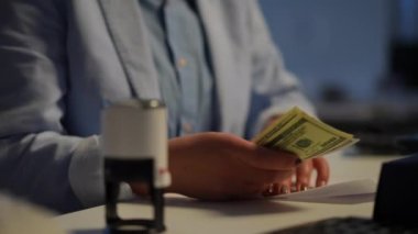 Unrecognizable woman putting cash inside sealing envelope stamping with seal. Young Caucasian worker sitting at table in office indoors with money. Income and profit concept
