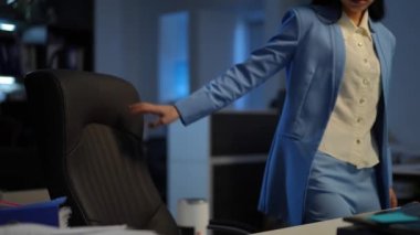 Young Asian woman entering office sitting down at table opening laptop checking e-mail. Portrait of confident positive smiling female manager at workplace indoors in the morning