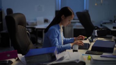Side view portrait of busy thoughtful Asian young woman typing on laptop keyboard sitting at table in office. Slim charming worker thinking analyzing e-market surfing Internet. Planning and business
