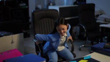 Joyful satisfied Asian woman spinning on chair in office in the evening smiling. Portrait of happy confident smart manager enjoying flexible schedule. Lifestyle and business concept