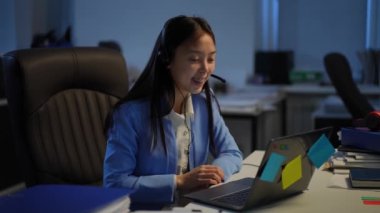 Charming positive Asian woman waving greeting in video chat on laptop talking. Portrait of confident smart female manager chatting online in office. Modern technologies and business