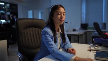 Side view young Asian woman sitting at table in office receiving document smiling. Thankful beautiful slim manager analyzing paperwork indoors in the evening. Business and lifestyle