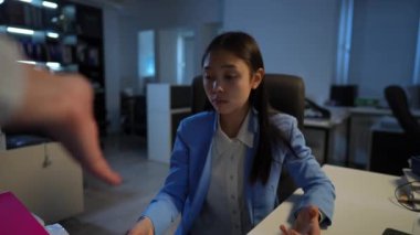 Portrait of sad stressed Asian young woman excusing herself for failures sitting in office at table with unrecognizable manager scolding gesturing. Incompetent employee apologizing for mistakes