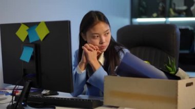 Thoughtful Asian young woman sitting at computer in office taking box with staff leaving. Portrait of fired confident female employee walking away indoors. Life change concept