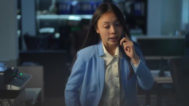 Nervous troubled young Asian woman talking on phone walking side to side persuading to sign the contract. Portrait of worried female manager convincing in business profitability strolling in office