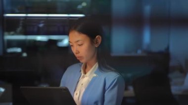 Concentrated young Asian woman working in office with female hand touching blinders at front spying. Unknown boss peeping after employee indoors