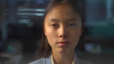 Headshot portrait of Asian woman behind glass with blinders closing. Front view close-up of young female employee standing in office looking at camera hiding