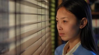 Close-up young Asian woman looking through window in office turning looking at camera smiling. Beautiful positive female manager with teeth braces posing at workplace in the morning