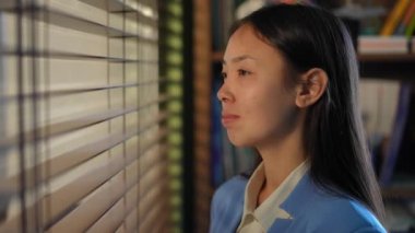 Side view portrait of positive Asian young woman looking out the window turning in slow motion looking at camera. Happy satisfied female employee posing in office in the morning
