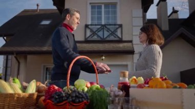 Side view happy loving Caucasian couple of farmers gesturing high-five hugging in slow motion on farm market. Positive smiling man and woman selling local fruits and vegetables on sunny day