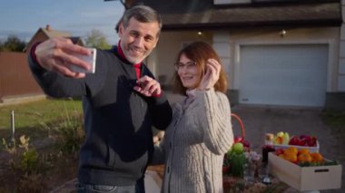 Adult couple of farmers blogging waving talking greeting subscribers standing on farm market outdoors. Positive happy Caucasian husband and wife advertising local organic products in social media