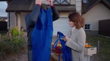 Side view portrait of Caucasian adult couple of farmers talking taking off aprons standing on farm market in the evening. Tired husband and wife discussing harvest and sales outdoors in slow motion