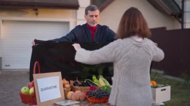 Focused man and woman covering vegetables and fruits on farm market with Quarantine placard on table. Sad concentrated Caucasian couple of farmers closing small business on coronavirus pandemic