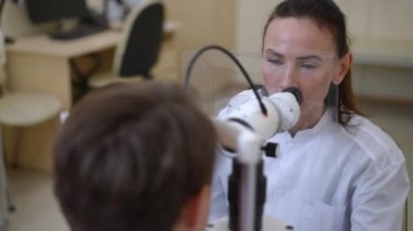 Portrait of professional concentrated woman examining man eye with slit lamp in hospital. Serious focused ophthalmologist doing medical examination of patient in medical clinic. Health care concept