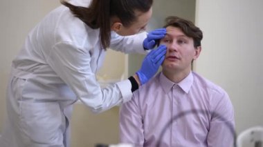 Concentrated doctor examining patient pupil visually in hospital. Professional Caucasian woman doing medical checkup of man talking to expert. Medicine and health care concept