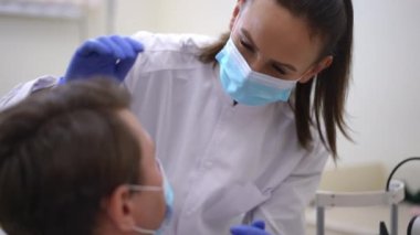 Portrait of woman in coronavirus face mask examining man eye visually in medical clinic talking smiling. Professional intelligent Caucasian doctor doing medical examination of patient in hospital