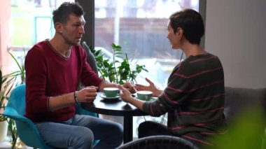 Concentrated man talking with woman in cafe calming down partner smiling. Portrait of loving caring Caucasian adult boyfriend taking girlfriend hands comforting lady. Support and understanding concept