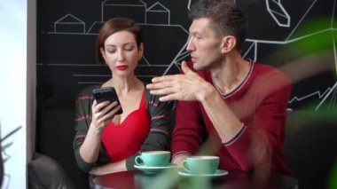 Selfish woman surfing Internet on smartphone ignoring man sitting in cafe. Sad Caucasian adult boyfriend sighing looking away as arrogant girlfriend disregarding partner. Bad date concept