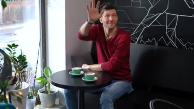 Excited man waving greeting woman in cafe as lady entering hugging kissing spouse. Portrait of happy loving Caucasian handsome husband dating with beautiful wife on weekend