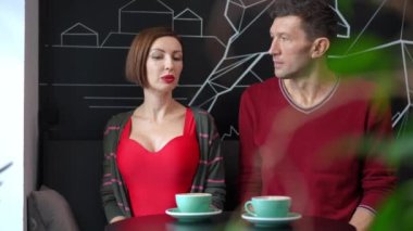 Front view confident couple talking hugging and smiling sitting in cafe. Loving Caucasian handsome man and attractive woman embracing dating indoors looking out the window