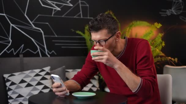 Joyful Carefree Man Eyeglasses Surfing Internet Smartphone Laughing Drinking Cappuccino — Vídeos de Stock