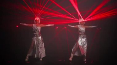 Wide shot confident female performers in costumes with red neon light dancing at black background moving simultaneously. Slim professional Caucasian dancers performing on stage with laser beam