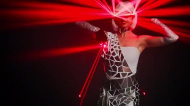 Smiling slim woman with neon light on eyeglasses posing performing modern dance on stage. Portrait of confident talented Caucasian female performer dancing at black background with laser beam