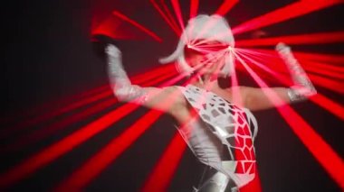 Gorgeous confident woman with toothy smile in cyber costume performing on stage looking at camera. Portrait of Caucasian female performer dancing at black background with laser beam on eyeglasses