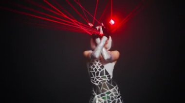 Zoom in to confident talented woman in cyber costume with red neon light dancing at black background. Live camera approaches to Caucasian female dancer performing modern art on stage