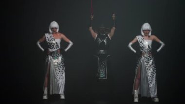 Wide shot professional performers standing on stage at black background as man turning on red neon light imitating swords. Dancer in samurai costume and women in futuristic outfit performing