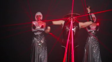 Front view professional dancers performing futuristic modern dance on stage at black background. Confident man in cyber samurai costume and women in white dresses with red laser beam dancing