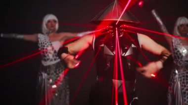 Medium shot of male dancer in samurai costume with face mask and neon light performing on stage. Blurred Caucasian female performers standing at background. Contemporary dance and art. Slow motion