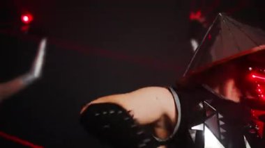 Man in samurai costume with red neon light on face mask performing contemporary dance in slow motion on stage. Portrait of male Caucasian performer dancing with blurred women at background