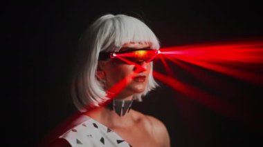 Headshot portrait of confident woman in eyeglasses with red laser light turning head standing at black background. Close-up of Caucasian female performer on stage in darkness