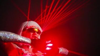 Professional talented dancer with red neon light on eyeglasses and gloves performing in slow motion on the left at black background. Portrait of confident Caucasian woman in futuristic costume dancing