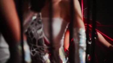 Unrecognizable women dancing in cage with man in cyber samurai costume sitting at background. Dancers performing on stage in futuristic outfit with red neon light laser beam. Slow motion