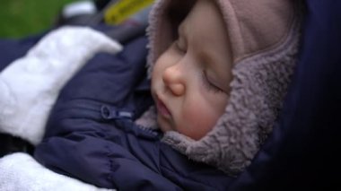 Panning from cute face of sleeping infant to tiny little hand of napping baby. Charming Caucasian newborn girl enjoying rest dreaming outdoors lying in baby stroller