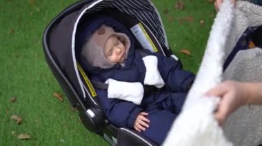 Zoom in to charming sleeping infant in baby stroller with female hands covering child with blanket. Cute little Caucasian girl napping on backyard outdoors with mother taking care of kid
