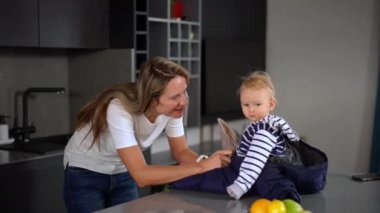 Curios charming Caucasian little girl looking at camera smiling as happy woman touching child nose raising kid. Pretty cute daughter enjoying leisure with mother indoors at home in kitchen