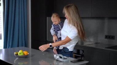 Side view positive happy mother showing green apple to child talking with baby girl. Caucasian woman chatting with infant standing at home in kitchen in the morning. Healthy eating and motherhood