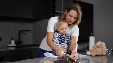 Positive Caucasian woman slicing lemon on cutting board with knife giving slice for infant to taste. Portrait of curios cute baby girl trying sour fruit sitting on tabletop in kitchen with mother