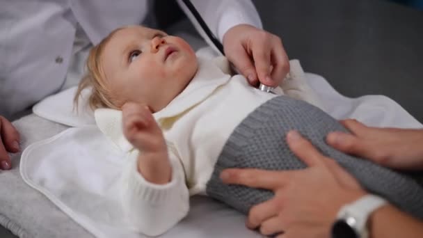 Cute Caucasian Infant Looking Doctor Using Stethoscope Unrecognizable Mother Stroking — стокове відео