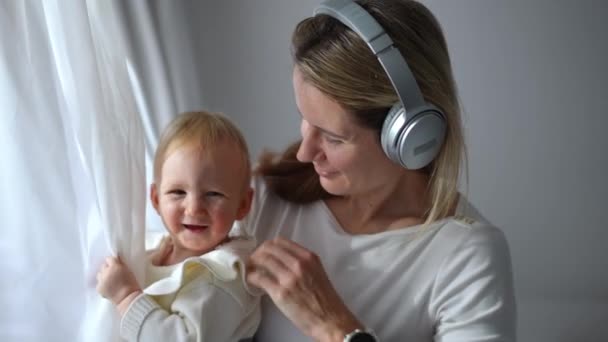 Happy Smiling Mother Headphones Looking Out Window Caressing Head Joyful — Αρχείο Βίντεο