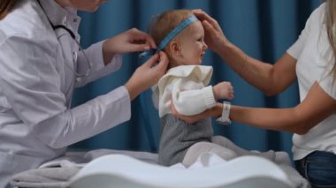 Side view portrait of female toddler sitting in hospital looking up at woman as professional doctor measuring head circumference in slow motion. Carefree Caucasian baby girl on pediatrician visit