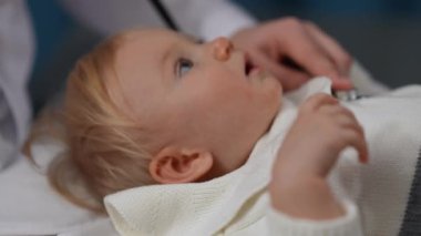 Düşünceli meraklı küçük kız yavaş çekimde steteskop kullanarak tanınmayan doktora bakıyor. Pediyatri kliniğinde, profesyonel pediyatriste muayene olan Kafkas bebek.