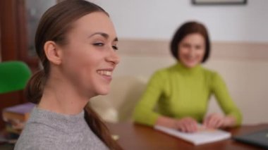 Arka planda oturan bulanık psikologla kameraya bakıp gülümseyen tatmin olmuş kadın hasta. Solda solda poz veren mutlu beyaz kadın portresi.