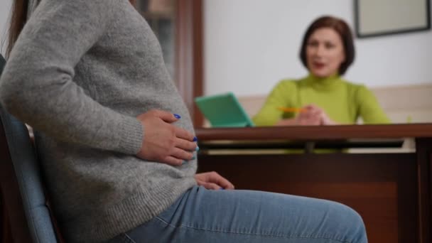 无法辨认的孕妇在左边抚摸着肚子 模糊的心理治疗师坐在后面说话 年轻的白种人病人在室内咨询专业专家医生 — 图库视频影像
