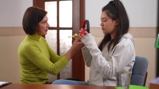 専門の精神療法士は 問題解決の助けを話して不安患者を強調するためにヘッドフォンを渡します Side Viewアジアのティーン女の子置きますオンイヤホンチャットとともに白人医師 — ストック動画