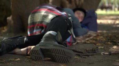 Açık havada, ağaçların altında yatan evsiz genç bir kadının yakın plan deri çizmesi. Bulanık Kafkas Çaresiz Evsiz Şehir 'de