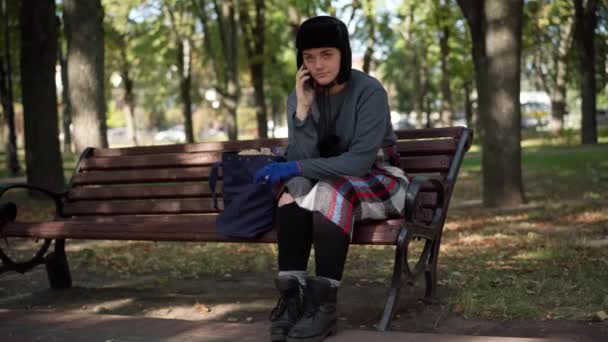 在公园的长椅上 有一张关于无家可归妇女在电话中交谈的全景肖像画 在阳光明媚的夏日 年轻而悲伤的高加索游牧民族在户外 贫穷和社会危机概念 — 图库视频影像